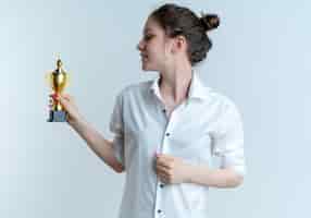 Free photo young pleased blonde russian girl holds and looks at winner cup isolated on white background