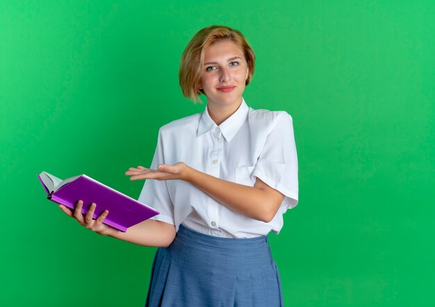 young pleased blonde russian girl holds and points at book