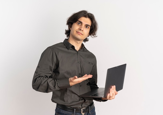 Молодой довольный красивый кавказский мужчина держит и указывает на ноутбук, изолированные на белом фоне с копией пространства