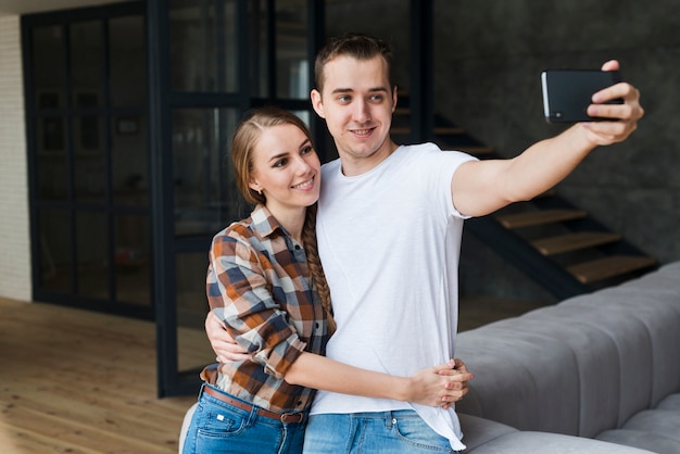 Young positive couple taking selfie in room at home