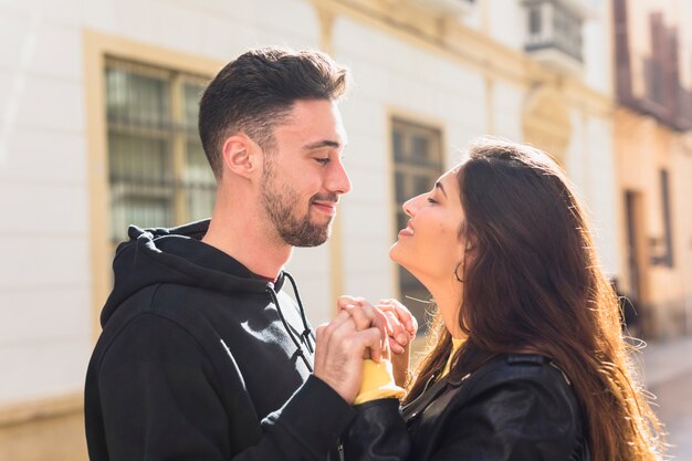 Young positive guy and happy lady holding hands on street