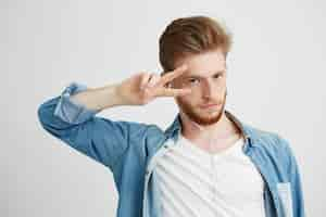 Free photo young positive handsome man in headphones listening to music dancing showing peace.