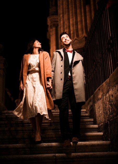 Young positive man holding hands with happy elegant woman on steps