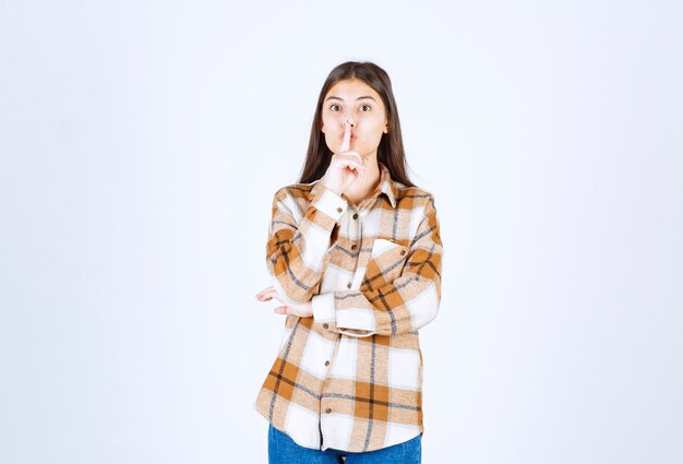 young positive woman giving silence sign on white wall. 