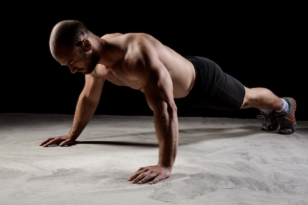 Young powerful sportsman training push ups over dark wall.