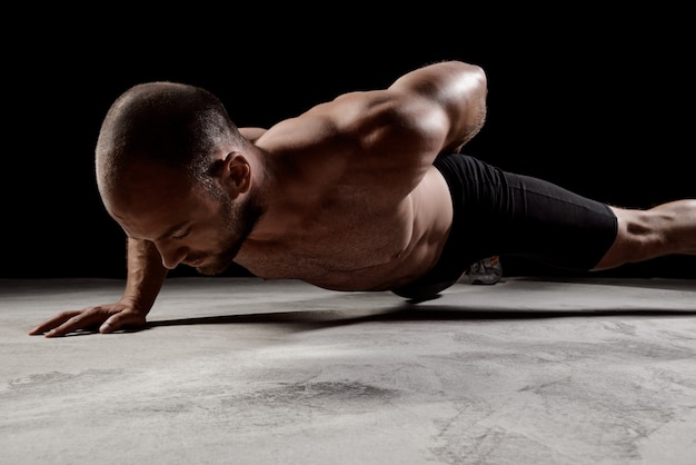 Free photo young powerful sportsman training push ups over dark wall.