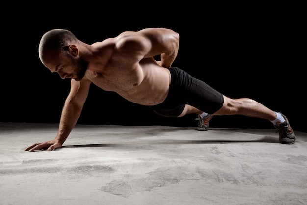 Young powerful sportsman training push ups over dark wall.