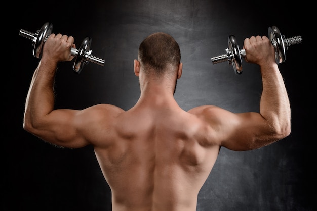 Free photo young powerful sportsman training with dumbbells over black wall.