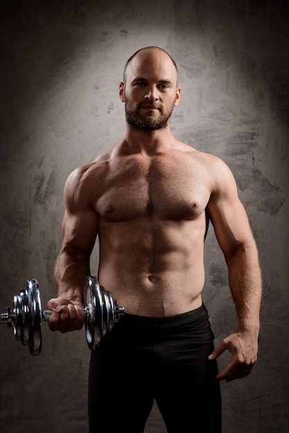 Free photo young powerful sportsman training with dumbbells over dark wall.