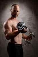 Free photo young powerful sportsman training with dumbbells over dark wall.