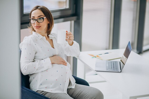 オフィスでコンピューターに取り組んでいる若い妊娠中のビジネス女性