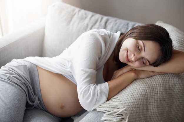 肘掛け椅子で寝ている若い妊娠中の女性