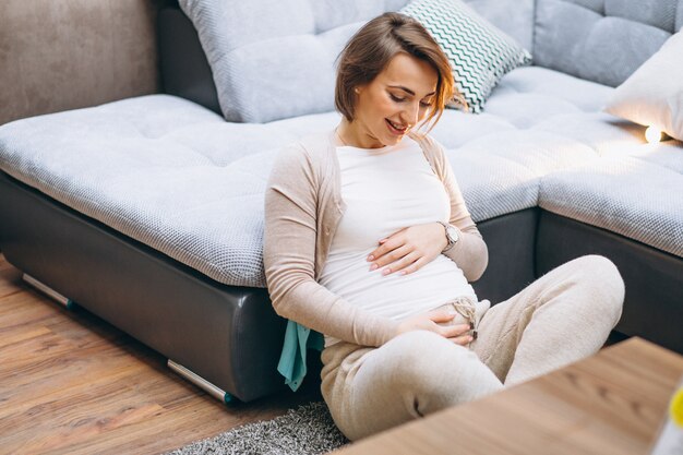 おなかを保持しているソファで自宅で若い妊娠中の女性