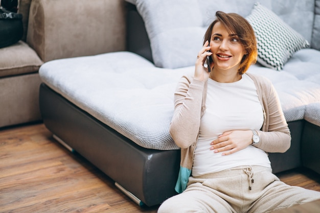 おなかを保持しているソファで自宅で若い妊娠中の女性