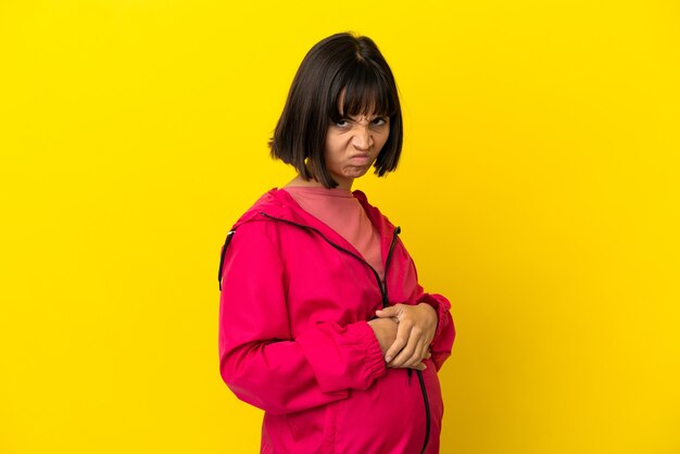 Молодая беременная женщина на изолированном желтом фоне, расстроенная