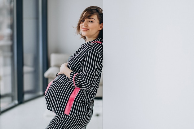 Young pregnant woman in pajamas at home by the window