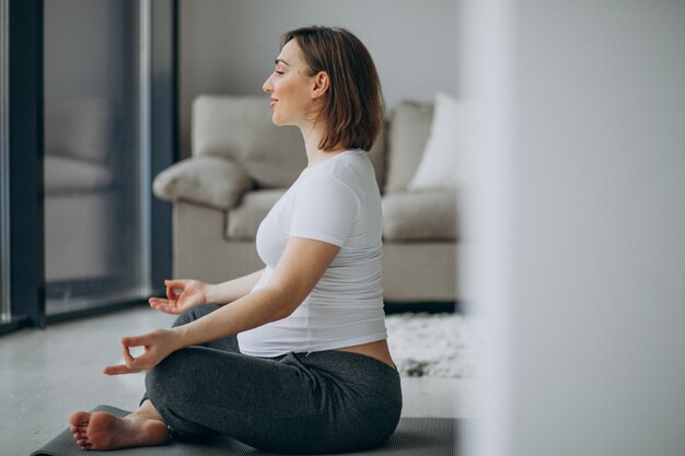 Молодая беременная женщина практикующих йогу дома