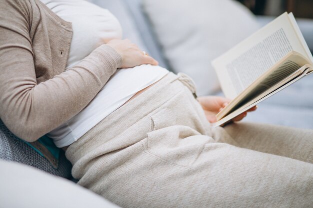 Young pregnant woman reading a book at home