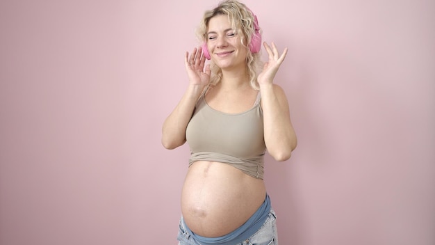 Free photo young pregnant woman smiling confident listening to music over isolated pink background