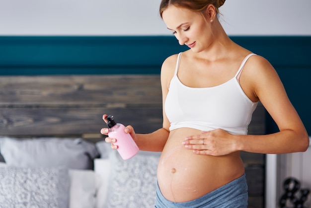 Free photo young pregnant women applying cream on her belly