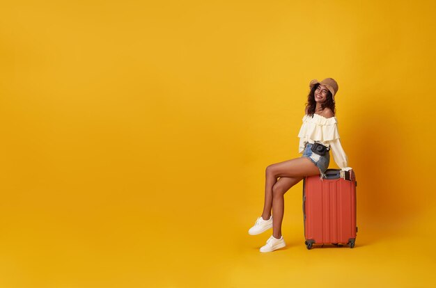 Young pretty african woman tourist smiling sitting on luggage with camera in hand