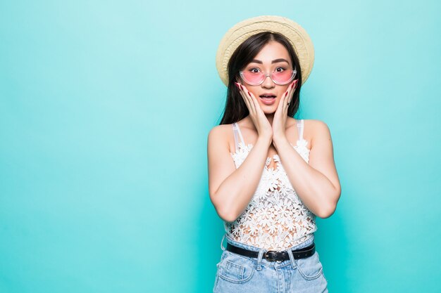 Молодая милая азиатская женщина удивленная при солнечные очки изолированные на зеленой стене