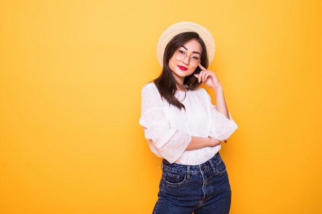 Young pretty asian woman with straw hat isolated on yellow wall