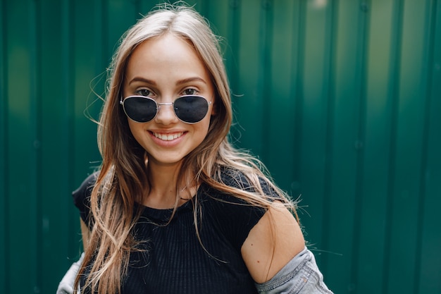 Young pretty attractive girl in denim clothes in glasses on a simple dark green wall with place for text.