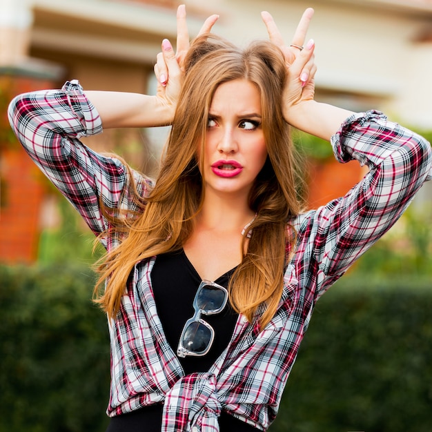 Young pretty blonde cheerful girl with grimaces face looking, posing in countryside in warm sunny spring day. Funny emotional face.