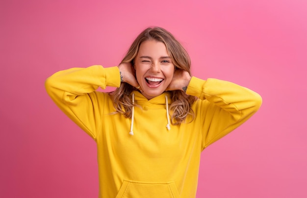 Free photo young pretty blonde woman cute face expression posing in yellow hoodie on pink bright background isolated emotional funny