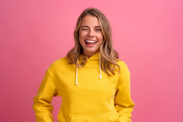 Young pretty blonde woman cute face expression posing in yellow hoodie on pink