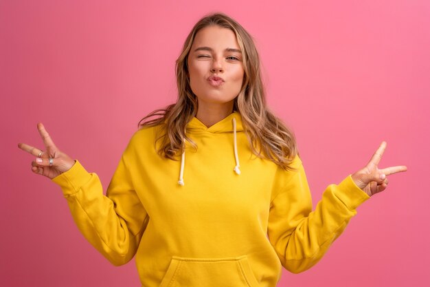 Young pretty blonde woman cute face expression posing in yellow hoodie on pink