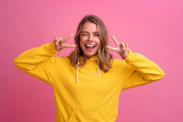 Young pretty blonde woman cute face expression posing in yellow hoodie on pink