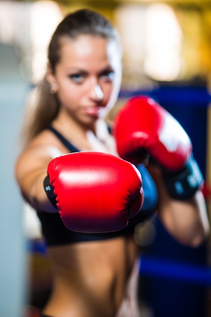 Young pretty boxer woman standing on ring and doing exercise with punching bag