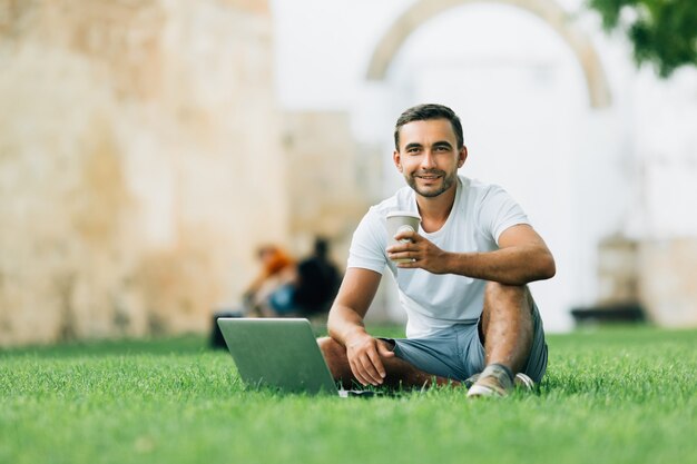 Young pretty boyfriend student sitting on a grass in a campus