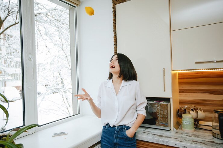 Free Photo young and pretty brunette standing by the window in the kitchen with lemon