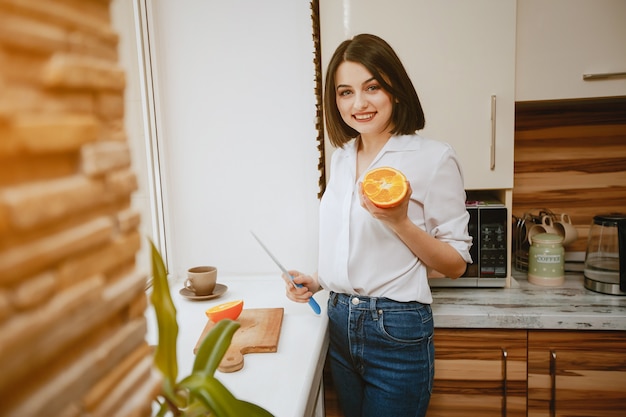 young and pretty brunette standing by the window in the kitchen with orange