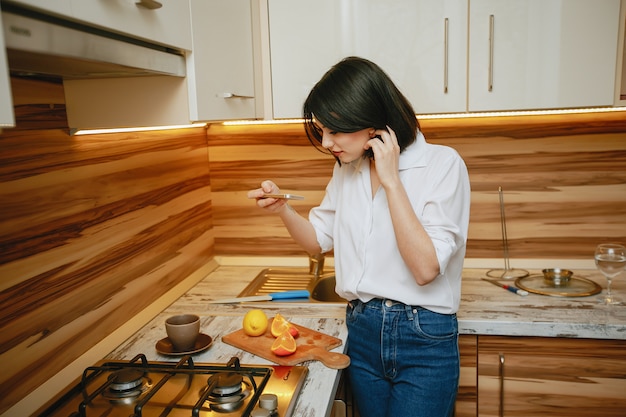 Free photo young and pretty brunette standing in the kitchen with phone