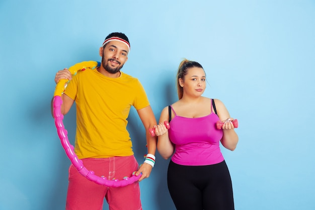 Free photo young pretty caucasian couple in bright clothes training on blue space concept of sport, human emotions, expression, healthy lifestyle, relation, family