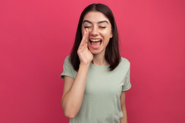 Young pretty caucasian girl keeping hand near mouth calling out to someone with closed eyes 