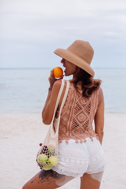 Free photo young pretty caucasian tanned fit woman in knitted clothes and hat on beach
