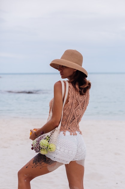 Young pretty caucasian tanned fit woman in knitted clothes and hat on beach