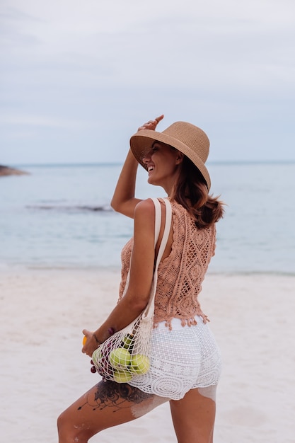 Молодая красивая кавказская загорелая женщина в вязаной одежде и шляпе на пляже