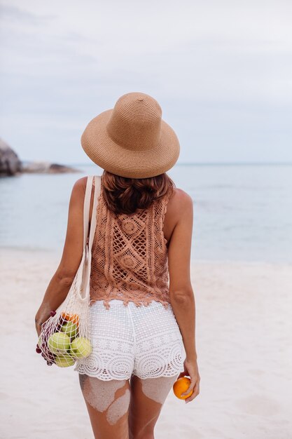 Young pretty caucasian tanned fit woman in knitted clothes and hat on beach