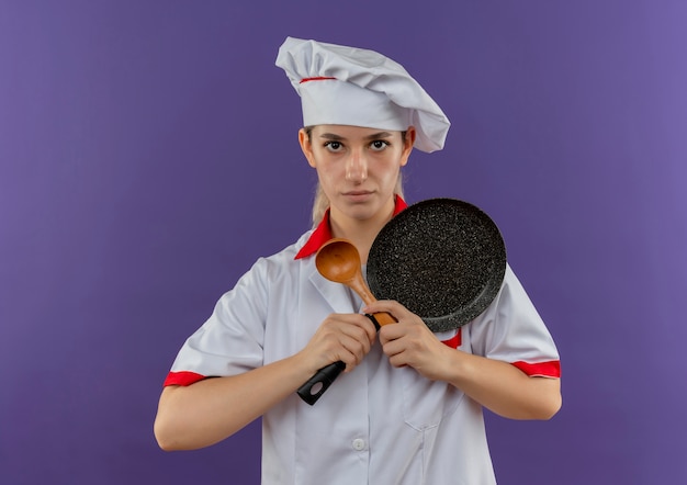 フライパンとスプーンを持ってシェフの制服を着た若いかわいい料理人