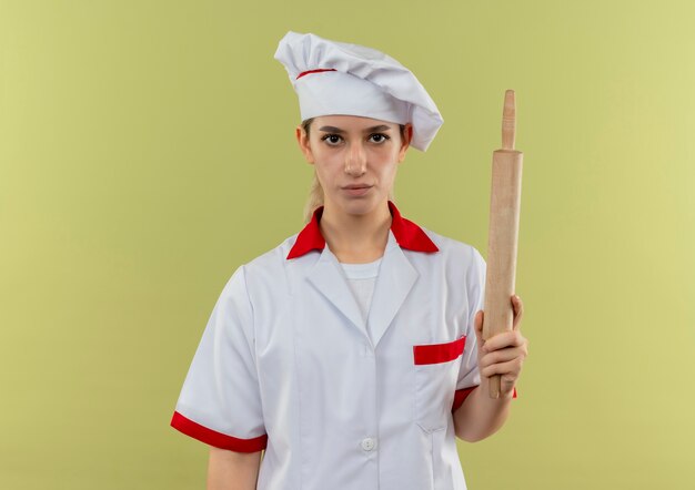 Young pretty cook in chef uniform holding rolling pin isolated on green background