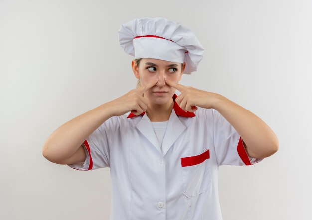 Free photo young pretty cook in chef uniform putting fingers on nose and looking at side