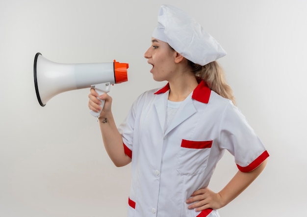 Young pretty cook in chef uniform talking by speaker looking at side with hand on waist