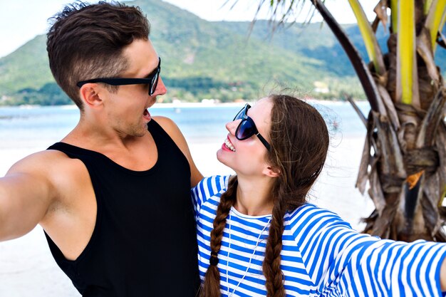 Young pretty couple of young travelers having fun and making selfies in tropical vacation