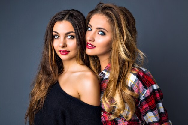 Young pretty couples of womans posing, fashion trendy elegant portrait, brunette and blonde, best friends hugs, color matching clothes, bright sexy make up, long hairs.